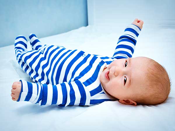 Cute little baby in bed wearing blue and white striped onesie.