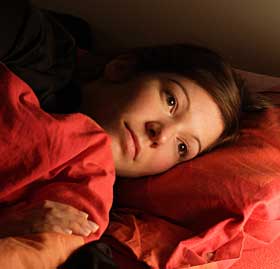 Lady with red blankets laying in bed with eyes open.