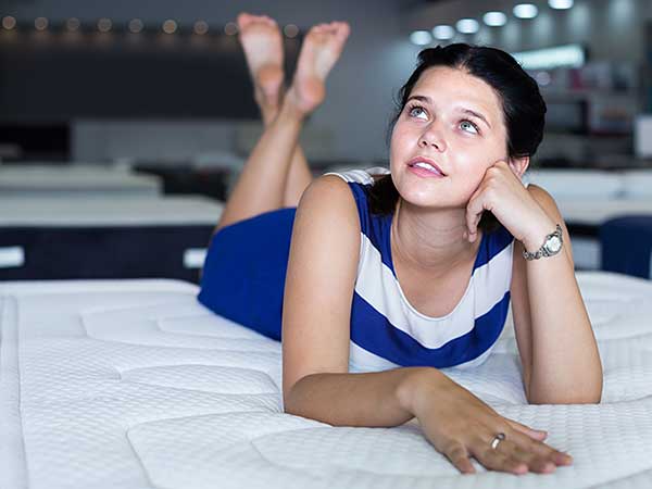 Lady in blue and white dress laying on mattress in store.
