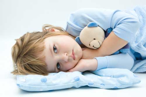 Child laying down hugging teddy bear.