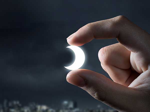 Photo illustration of moon between fingers.