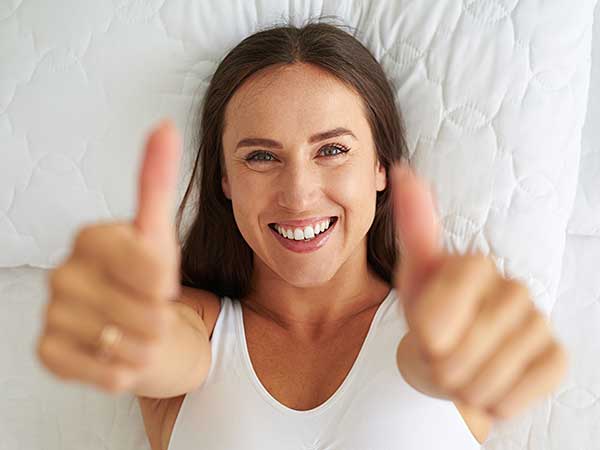 Lady laying on bed give two thumbs up.