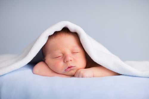 Newborn sleeping posed with blanket over head.