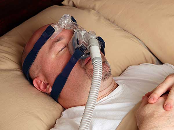 Man sleeping on back using sleep apnea equipment.