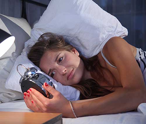 Woman with sleep manintenance insomnia looking at alarm clock