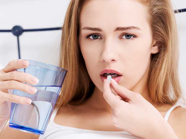 Woman with glass of water taking pill.